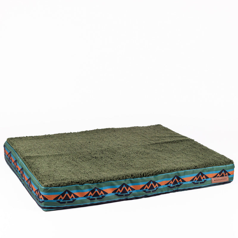 The Memory Foam Dog Bed - Replacement Waterproof Liner features a rectangular green design with a soft, textured surface and a blue, orange, and black geometric mountain side pattern, plus a non-skid bottom for secure placement.